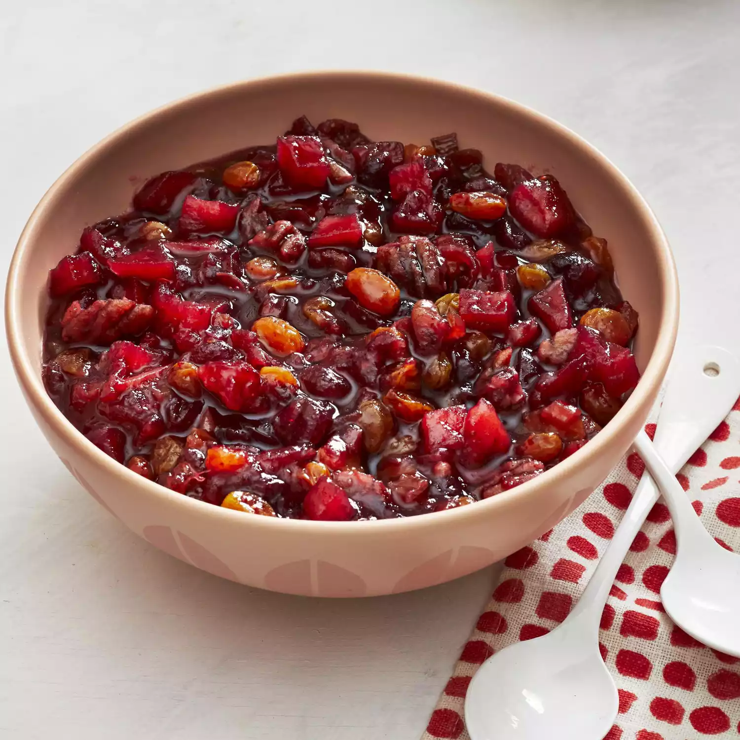 A peach colored bowl of chutney with a patterned red and white napkin alongside.