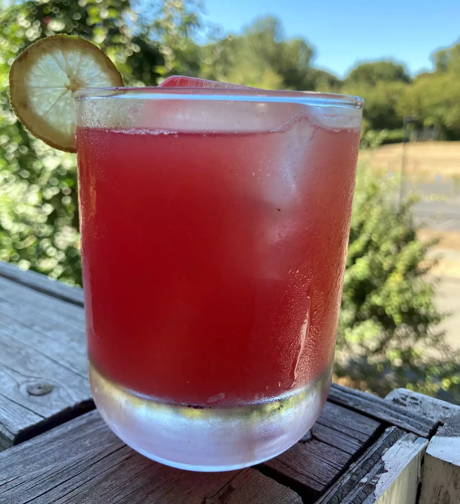 an iced glass of bright red watermelon drink with condensation on the glass, garnished with a lime wheel