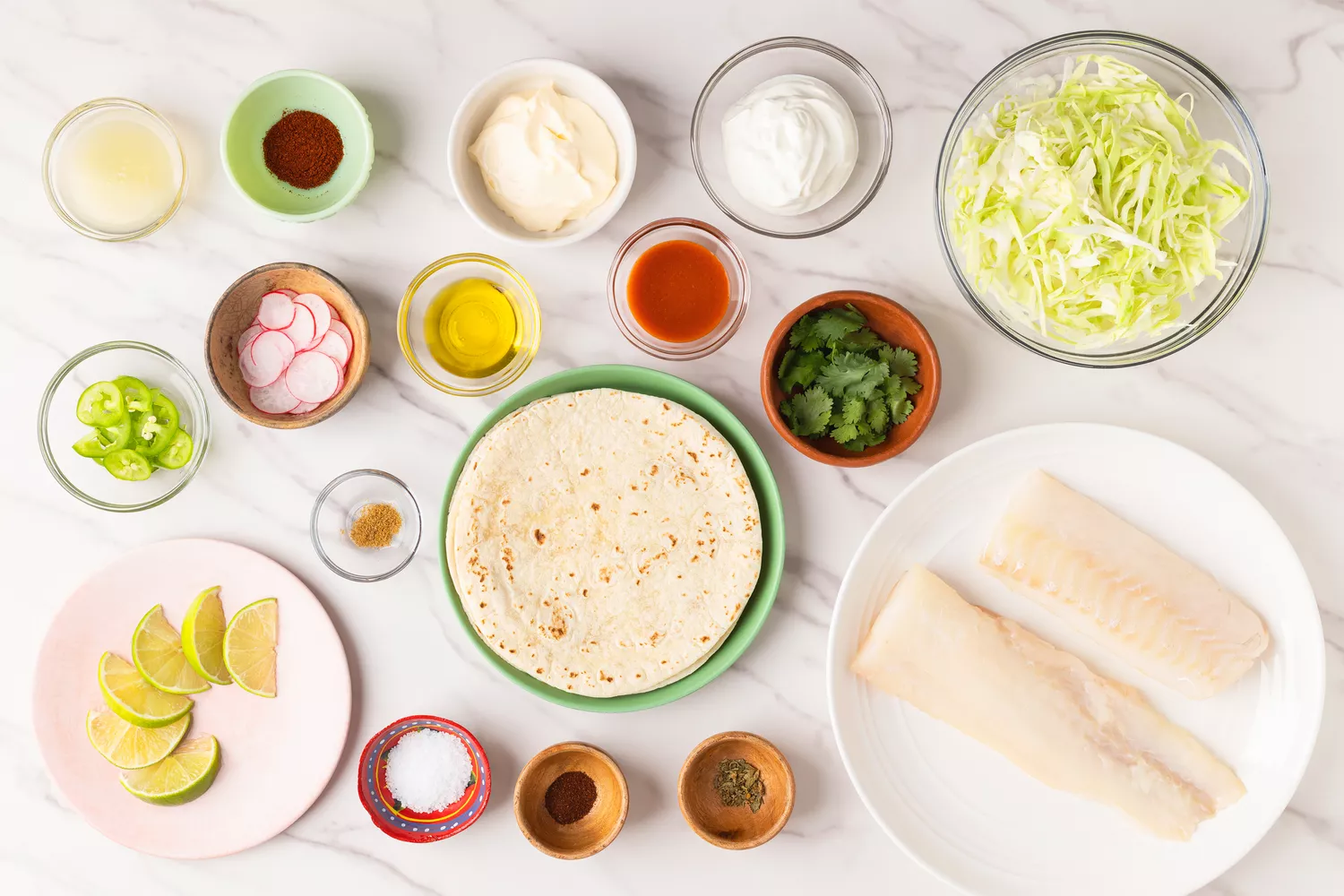 Various bowls and plates filled with ingredients to make baked puffy fish tacos. 