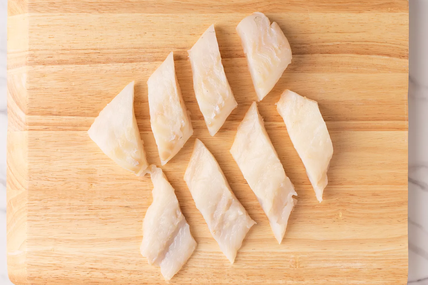 Uncooked fish pieces on a wood cutting board.