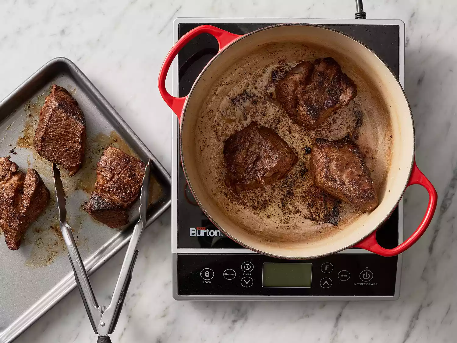 Overhead of cooked beef in a dutch oven with pieces being transferred to a baking sheet. 