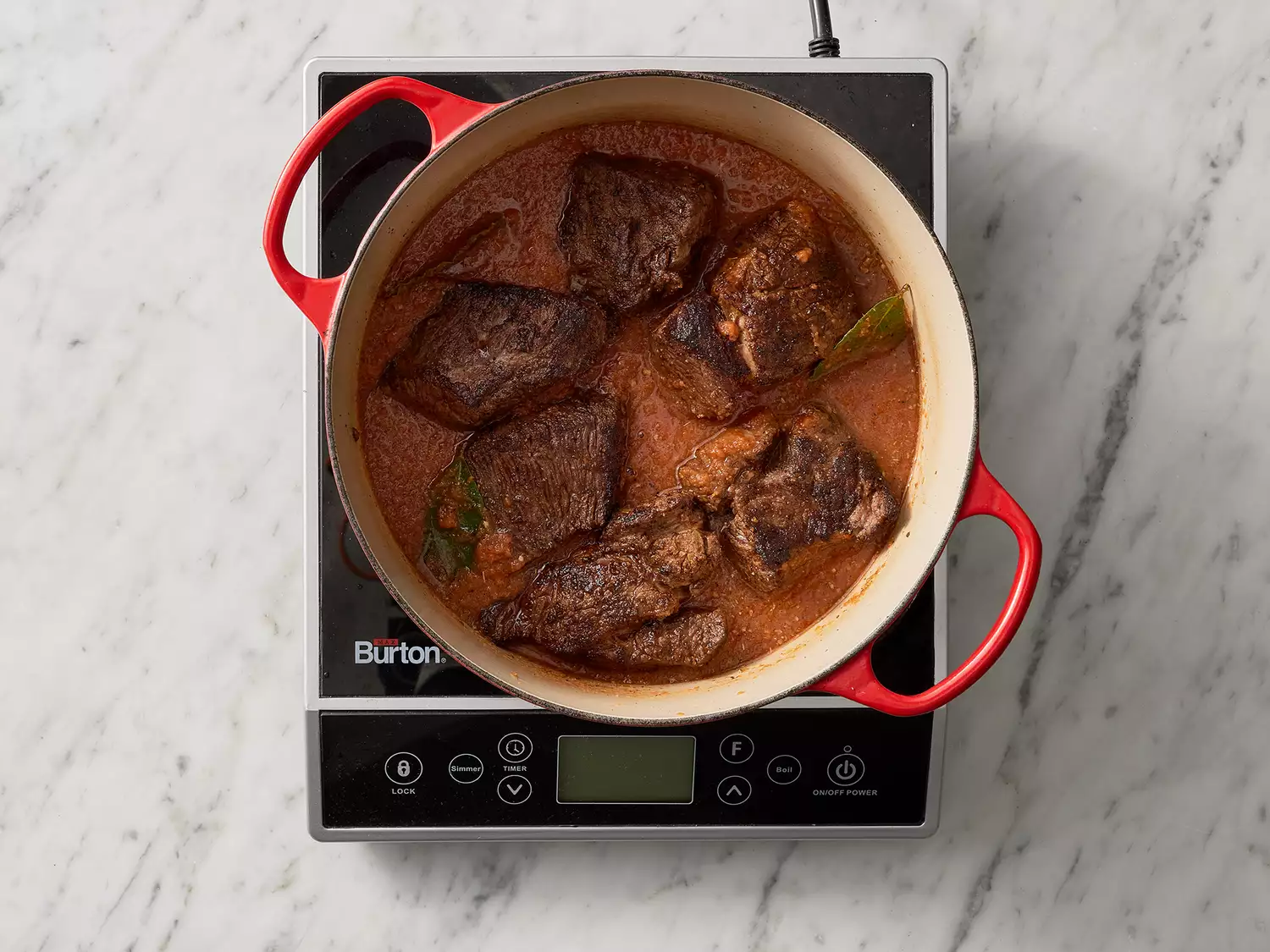 Overhead of a dutch oven with beef cooking in a sauce mixture.